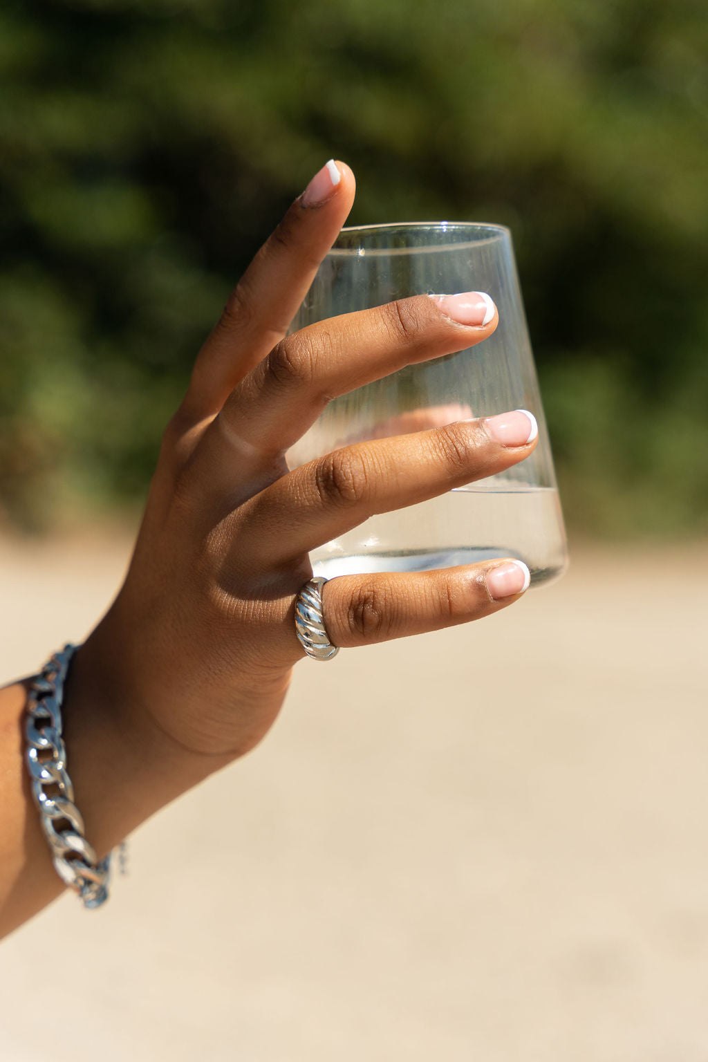 Model holding a glass of water. She is wearing a 18k silver croissant shaped ring. She is also wearing a silver chain bracelet. Thick Croissant Rings by E's Element.