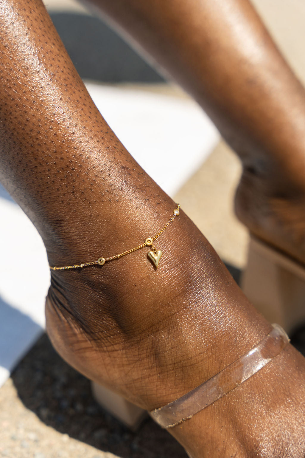 Model wearing an 18k gold anklet with a heart shaped charm. Ella's Element Heart Charm Anklet by E's Element.