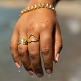 Model in a black top wearing 18k gold heart shaped ring. The model is also wearing another 18k gold ring on the ring finger and a chain bracelet. Ella's Element Hollow Heart Out Ring by E's Element.