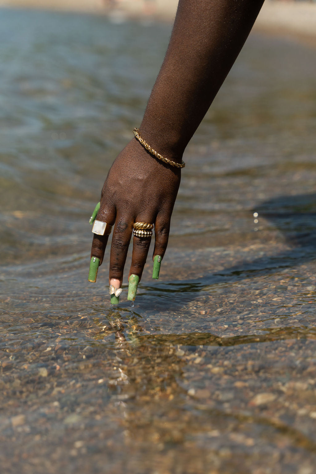 Model wearing 18k gold ring dipping her hands in water. . The ring has a shell attached. She is also wearing a gold bracelet and a gold and silver ring on her ring finger. Shell Signet Ring by E's Element.