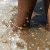Legs with 18k gold stainless steel anklets worn on them and submerged under water.