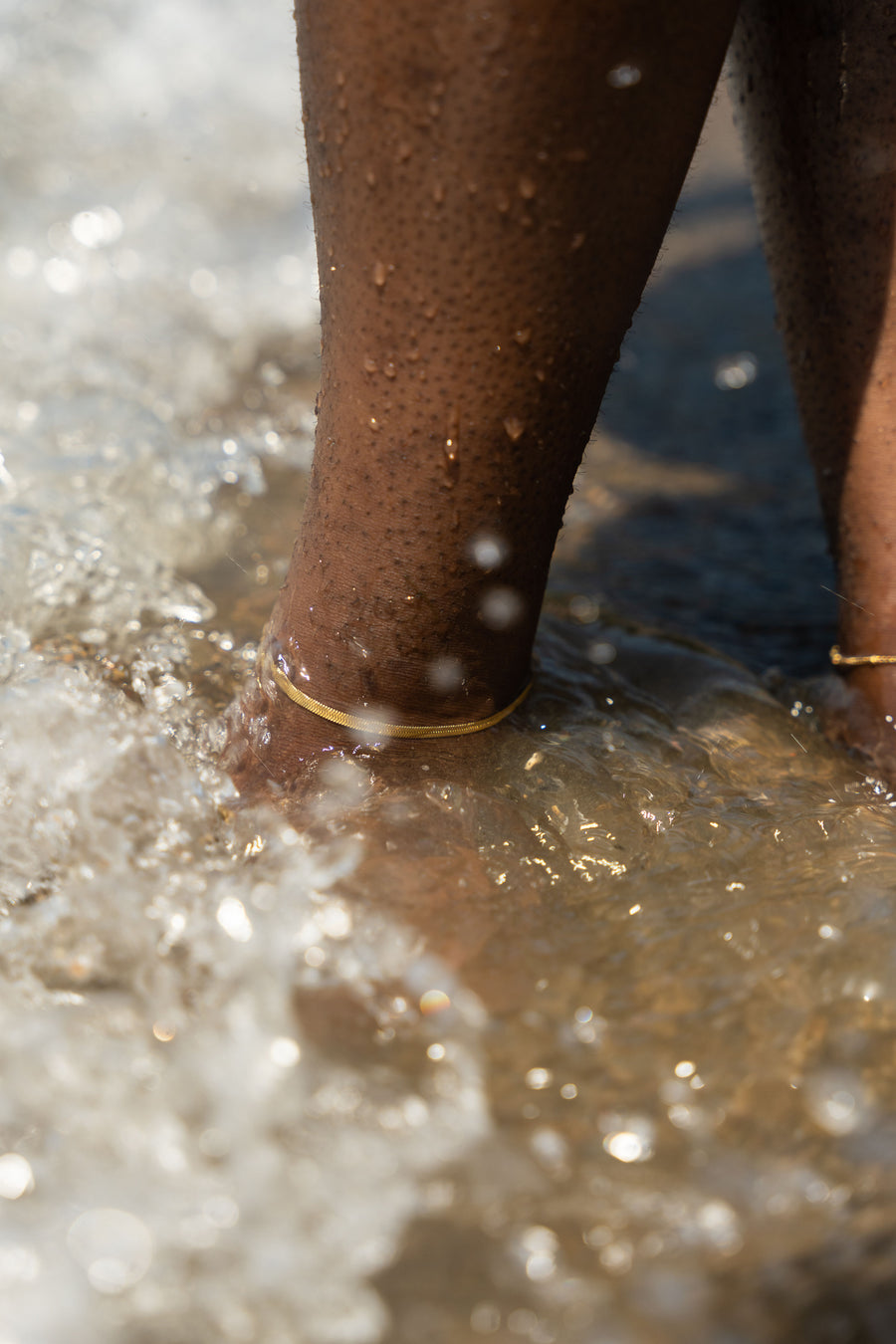 Legs with 18k gold stainless steel anklets worn on them and submerged under water.