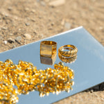 Two 18k gold stainless steel rings and a necklace resting on top of a mirror. Build Your Own Jewelry Set by E's Element.