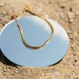 18k gold stainless steel anklet resting on top of a round mirror on the sand.