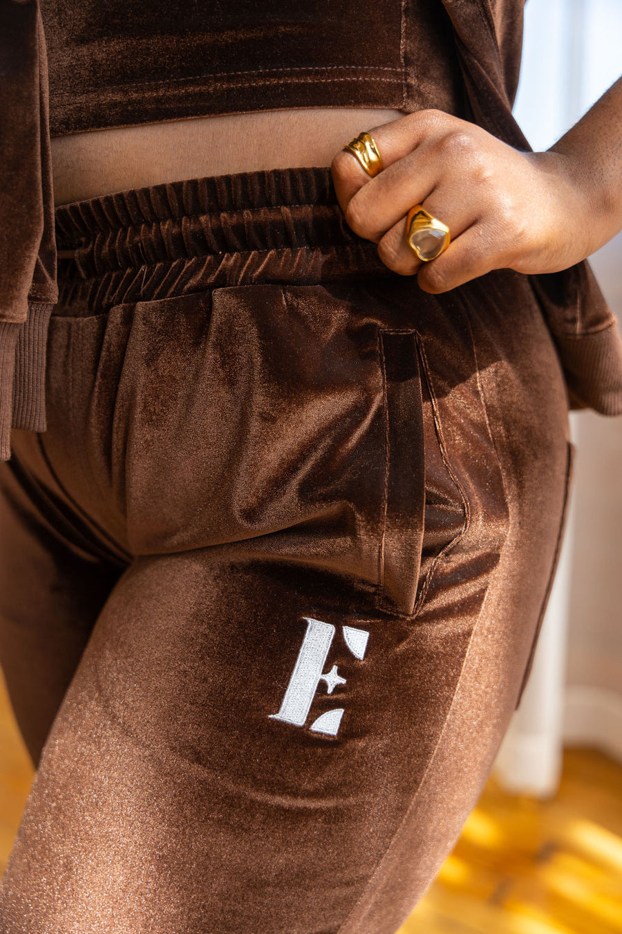 Model wearing dark brown crop top and joggers. The jogger has the E's Element logo imprinted in white. She is also wearing 18k gold rings on her index and ring finger. 