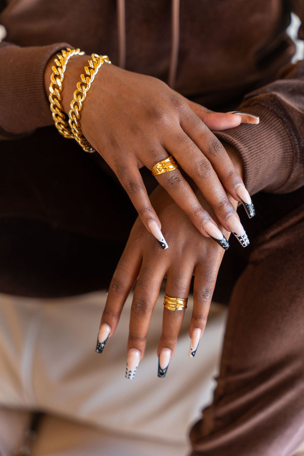 Model wearing dark brown sweat suit. On her ring fingers are 18k gold molten rings. Ella Lava Ring 2.0 by E's Element.