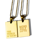Two 18K stainless steel gold necklaces. The words printed on one of the necklaces are, "THE WORLD IS YOURS" and "MORE SELF LOVE" on the other necklace.