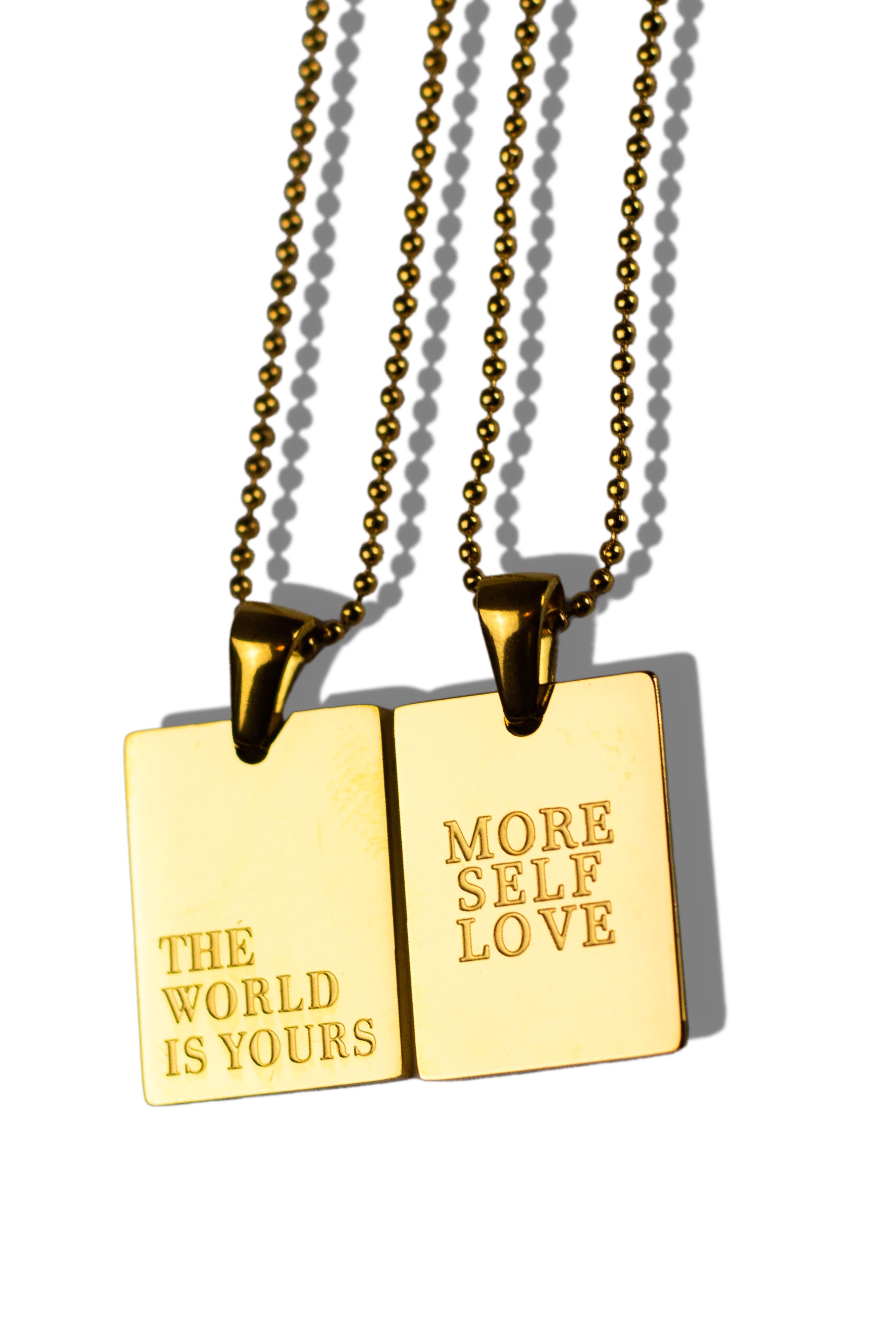 Two 18K stainless steel gold necklaces. The words printed on one of the necklaces are, "THE WORLD IS YOURS" and "MORE SELF LOVE" on the other necklace.