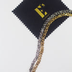 18k silver chain anklet and 18k gold chain anklet resting on a black polishing cloth with the E's Element logo imprinted in yellow. Ellina Link Chain Anklet by E's Element.