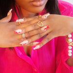 Model in a hot pink top wearing an 18k gold heart shaped ring. The model is also wearing rings on the index and ring finger. Ella's Element Hollow Heart Out Ring by E's Element.
