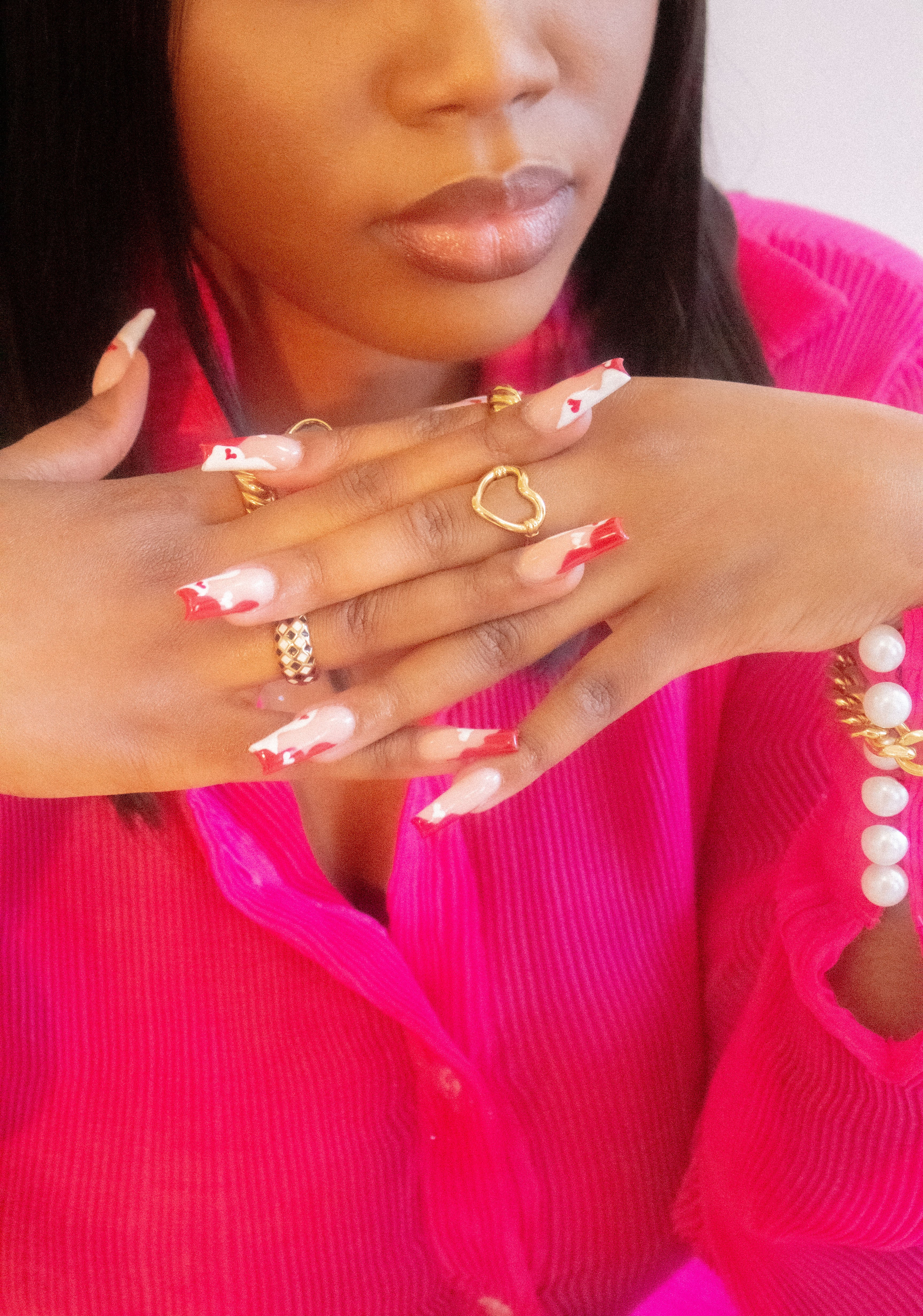 Model in a hot pink top wearing an 18k gold heart shaped ring. The model is also wearing rings on the index and ring finger. Ella's Element Hollow Heart Out Ring by E's Element.
