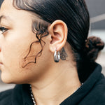 Woman in a black hoodie wearring 18K silver stainless steel hoop earrings. Named Alyssa Hoops by E's Element.