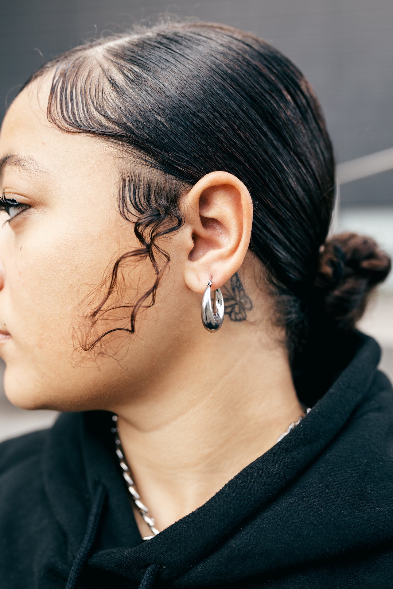 Woman in a black hoodie wearring 18K silver stainless steel hoop earrings. Named Alyssa Hoops by E's Element.