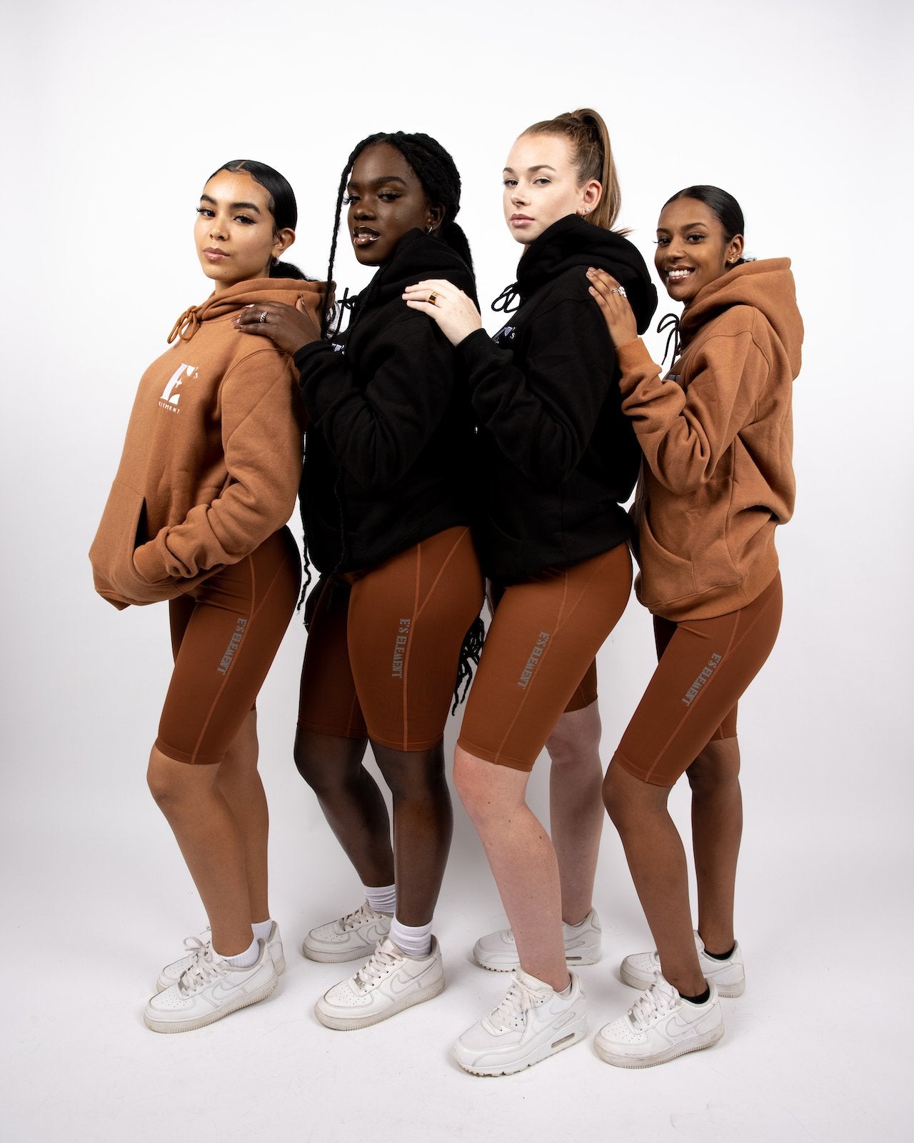 The models on the left and right are wearing brown hoodies. The two models in the middle are wearing black hoodies. All four models are wearing brown biker shorts and white sneakers. The Ella Shaping Cycling Shorts (Petite Size) by E's Element.
