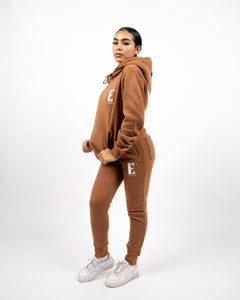 Model wearing a light brown sweat suit. The model is also wearing white sneakers. The sweat suit has the E's Element logo imprinted in white. E's Element Essential Brown Sugar Sweatsuit Set by E's Element.