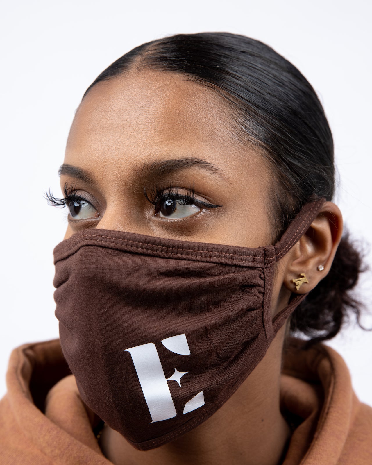 Woman in light brown hoodie wearing E's Element reusable face mask in brown. The face mask has E's Element logo imprinted in white. Build Your Own Reusable Masks by E's Element.