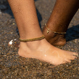 18k gold stainless steel anklets worn on the ankles submerged in water.