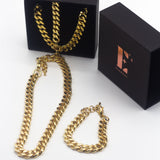 18k gold chain and necklace. On the left, the chain necklace and bracelet are placed in a black opened container. In front of the container is a gold chain necklace. On the right is the cap for the container with the E's Element logo imprinted in gold. Under the cap is a gold chain bracelet. The Emmanuela Set in Gold by E's Element.