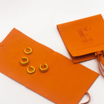 Two pairs of 18k gold cuff earrings resting on an orange leather envelope. There is another envelope on the right with the E's Element logo engraved.  Ellina Ear Cuffs by E's Element.