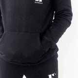 Model wearing a black sweat suit. The hoodie and sweat pants have the E's Element logo imprinted in white. E's Element Essential Smoky Black Sweatsuit Set by E's Element.
