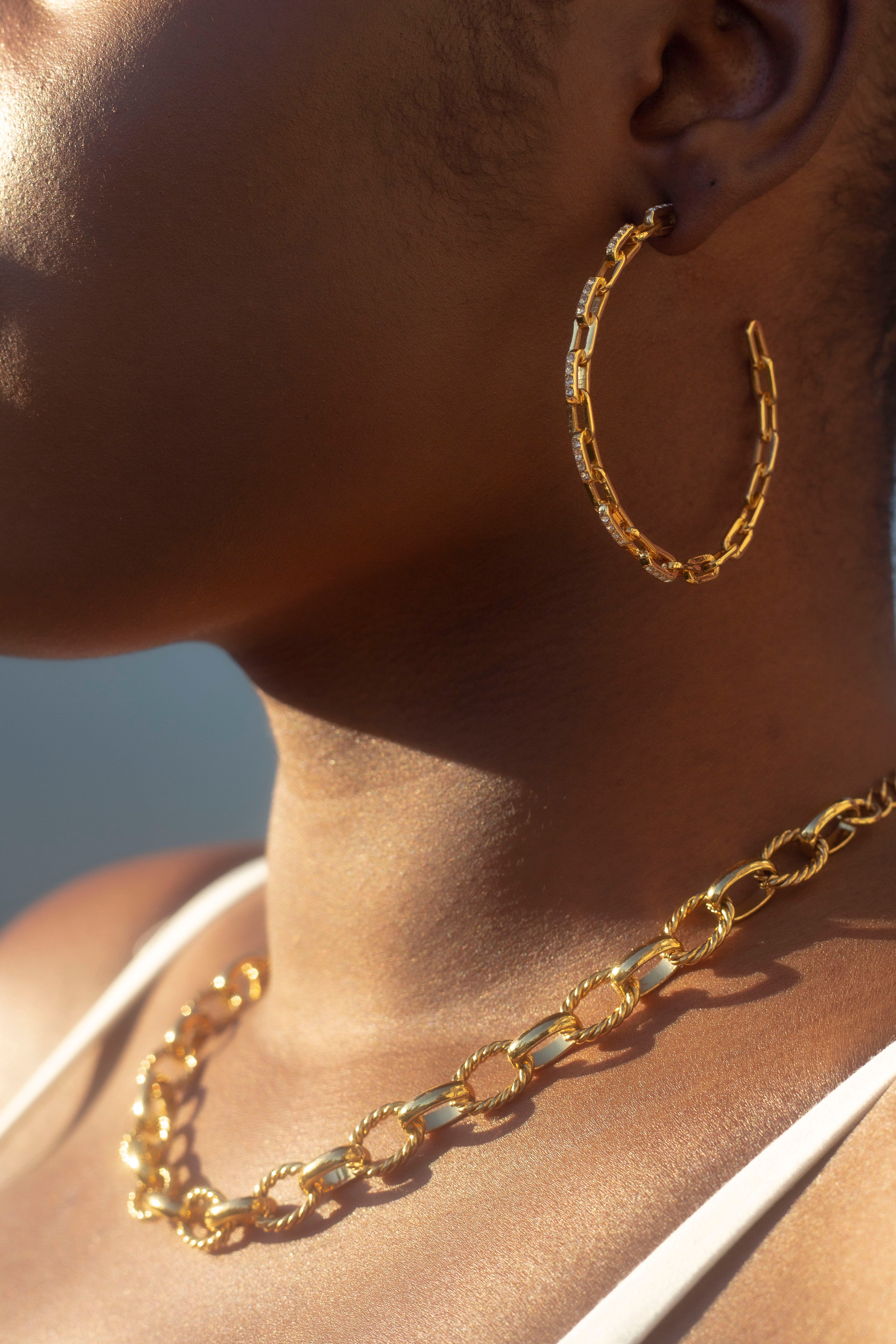 Side profile of model wearing 18k gold stainless steel cubic zircona earrings. The model is also wearing an 18k gold stainless steel necklace. Ella Anchor Cubic Zirconia Hoops by E's Element.