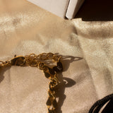 18k gold chain necklace placed on a beige cloth. Above the necklace is a white box. Ella Figaro Necklace by E's Element.