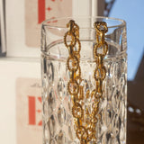 18k gold chain necklace with a rope pattern. The necklace is hanging on the edge of a glass cup. Rope Link Signature Chain by E's Element.