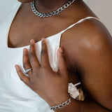 Model in a white dress wearing stainless steel chain necklace and bracelet. She is also wearing a steel ring and earring. The Emmanuela Set in Steel by E's Element.