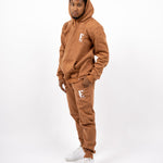 Model wearing a light brown sweat suit. The model is also wearing white sneakers. The sweat suit has the E's Element logo imprinted in white. E's Element Essential Brown Sugar Sweatsuit Set by E's Element.