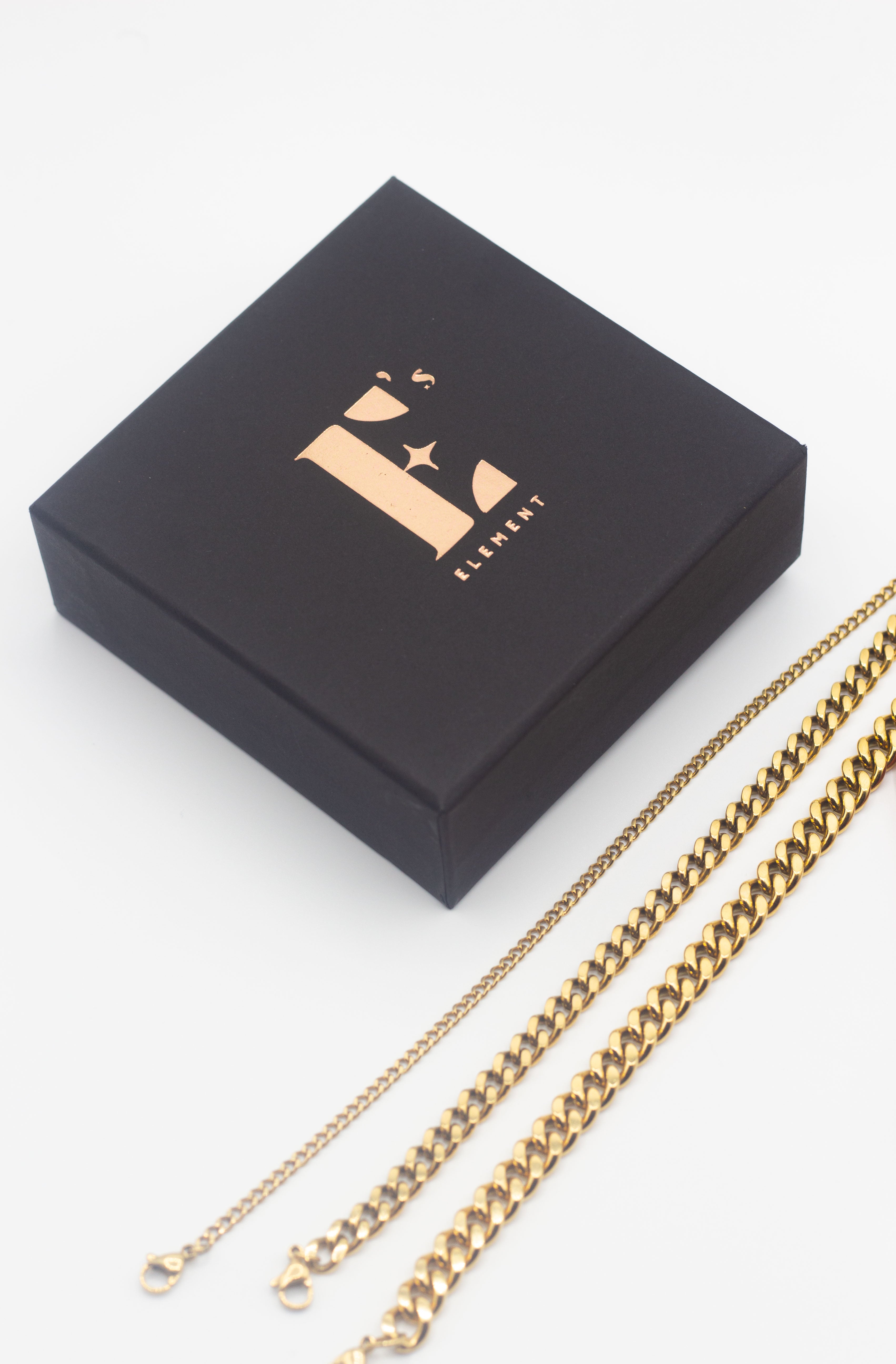 18k gold stainless steel chain anklets in three different sizes. Beside the anklets is the container for the anklets in black with E's Element logo engraved in gold.  Cuban Link Anklet by E's Element.