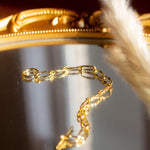 18k gold chain bracelet resting on a mirror with gold edges. The bracelet has a round hollow charm. Hollow Signature Chain Bracelet by E's Element by Emmanuela Okon.
