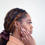 Side profile of model wearing 18k gold cuff earrings. The model is also wearing two other earrings and one of them has a cross charm. The model is also wearing rings on her fingers and a chain bracelet. Ellina Ear Cuffs by E's Element.