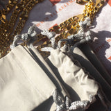 Grey cloth pouches stacked on each other. Above the pouches are 18k gold chains. Plain Grey Cloth Pouch by E's Element.