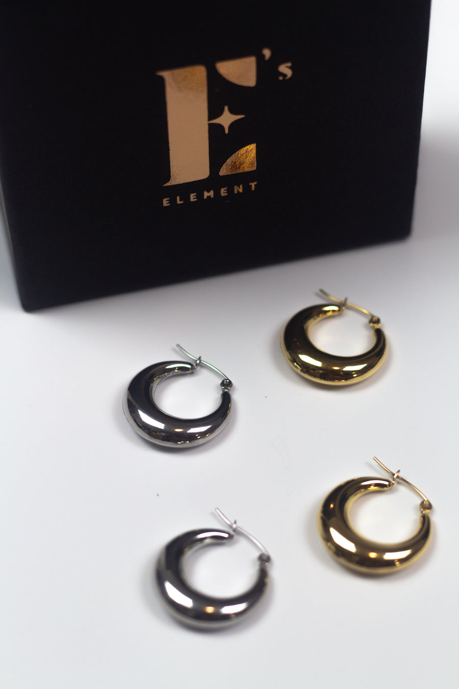 18k gold and silver stainless steel hoop earrings placed side-by-side. E's element container is above them. Alyssa Hoops by E's Element.