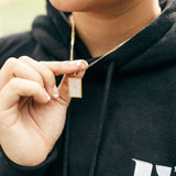 Model in a black hoodie wearing 18k gold necklace with a white rectangular charm. The hoodie has the E's Element logo in white. The Infinity Zircon Necklace by E's Element.