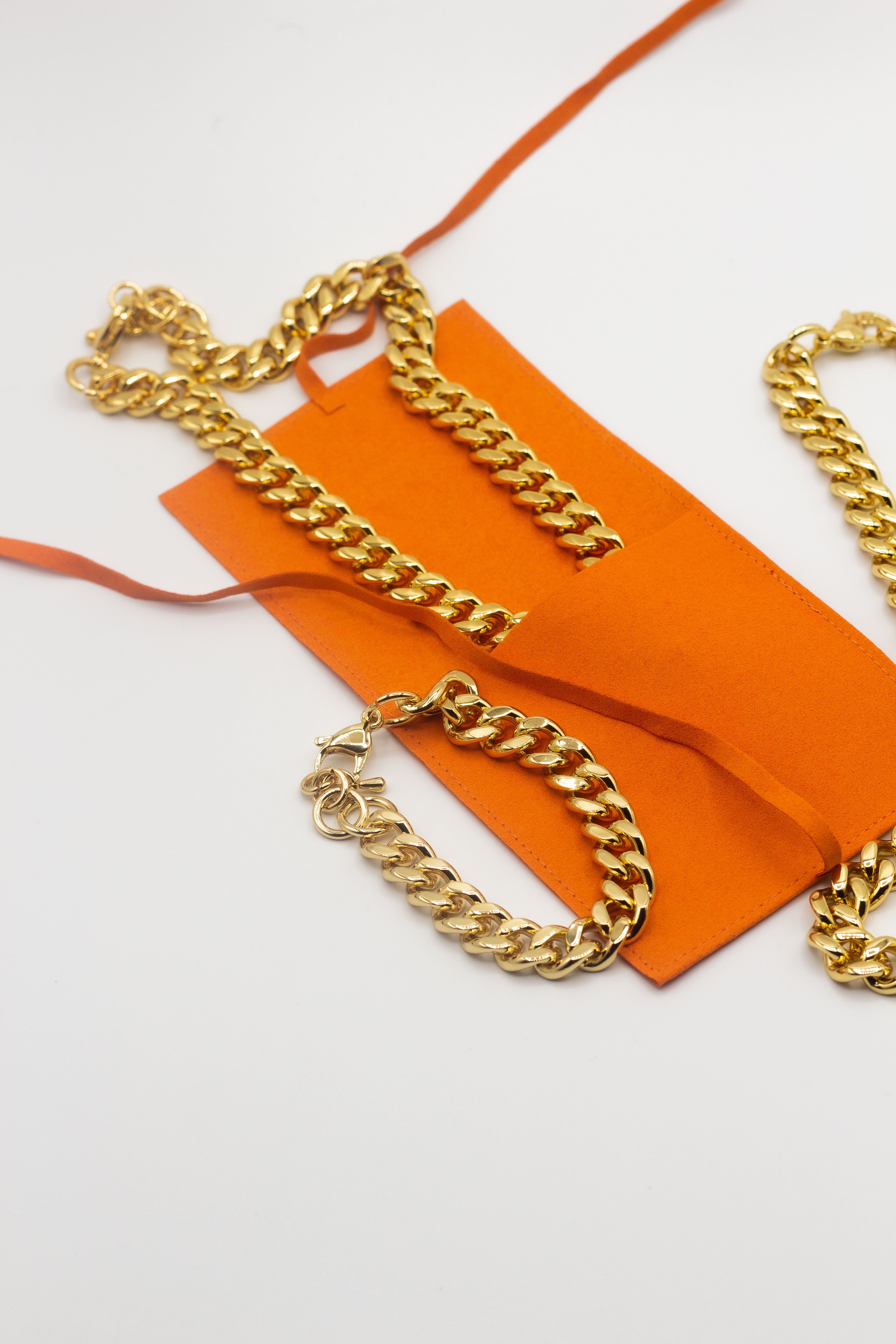 18k gold chain necklace resting inside an orange microfiber leather pouch. On the left is a gold chain bracelet and on the right is another gold chain necklace.  Microfiber Jewelry Pouch by E's Element