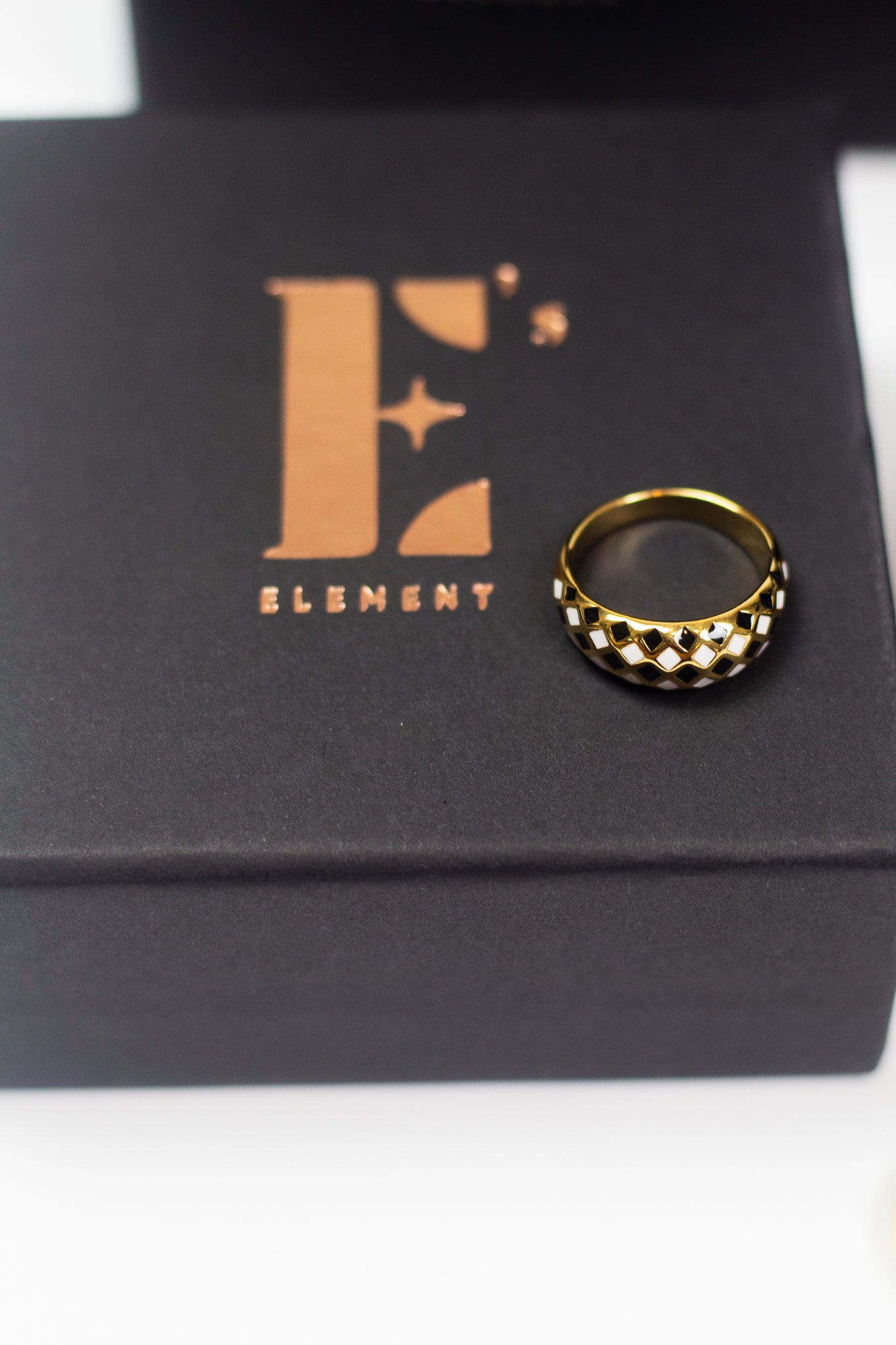 18k gold ring with black and white diamond dots. The ring is placed on a black container with E's Element logo imprinted in gold. Minimalist Resin Ring by E's Element.