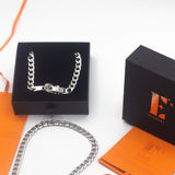 18k silver stainless steel buckle choker resting in its container. There is an orange leather packaging on the right and a lid with the E's Element logo imprinted. There is another silver buckle choker placed under the container with the choker. Ella Buckle Choker by E's Element.