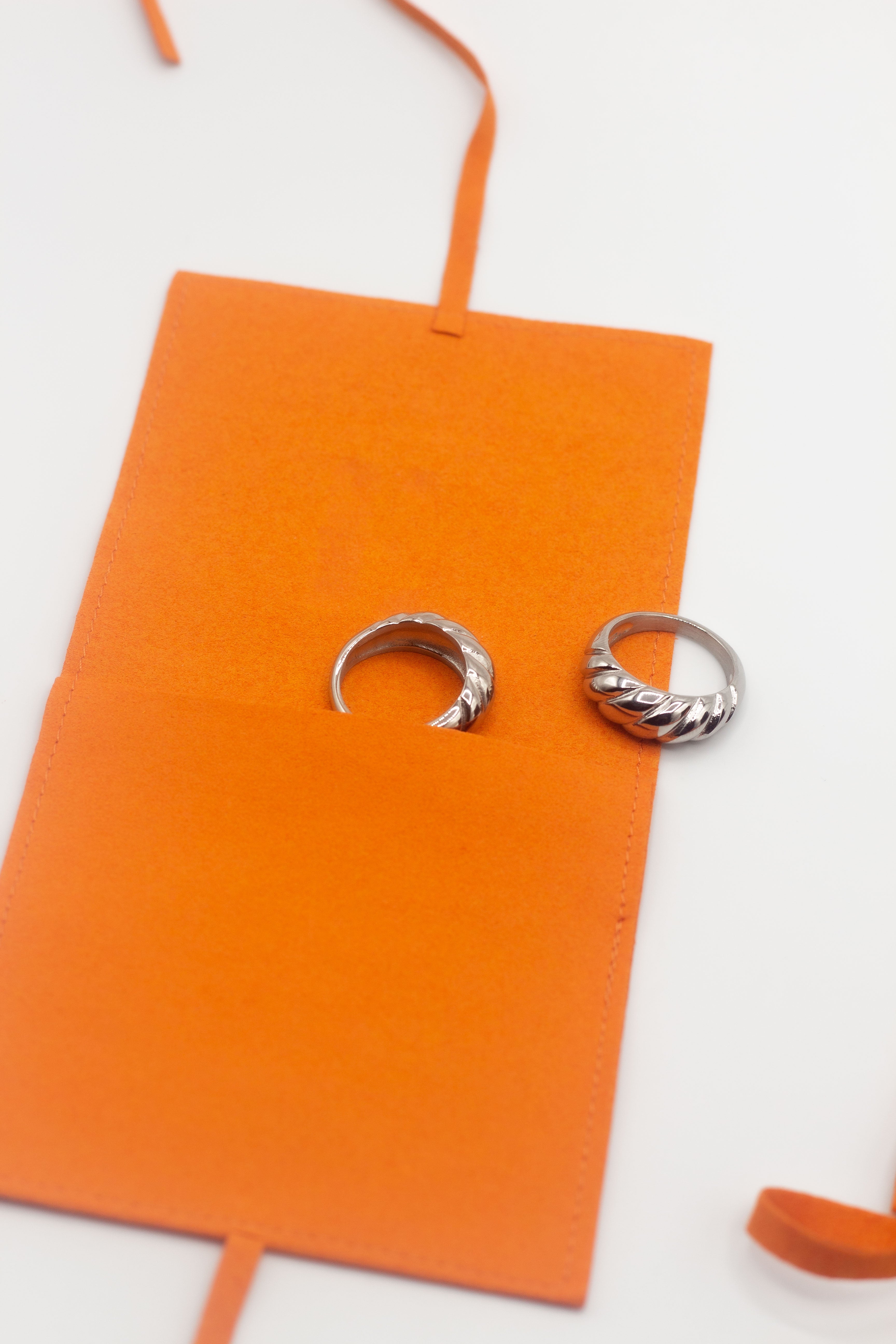 18k silver croissant shaped rings placed inside an orange leather pouch. Thick Croissant Rings by E's Element.