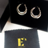 18K silver stainless steel hoop earrings in its container. There is a polishing cloth underneath with E's Element logo printed in yellow. Alyssa Hoops by E's Element.