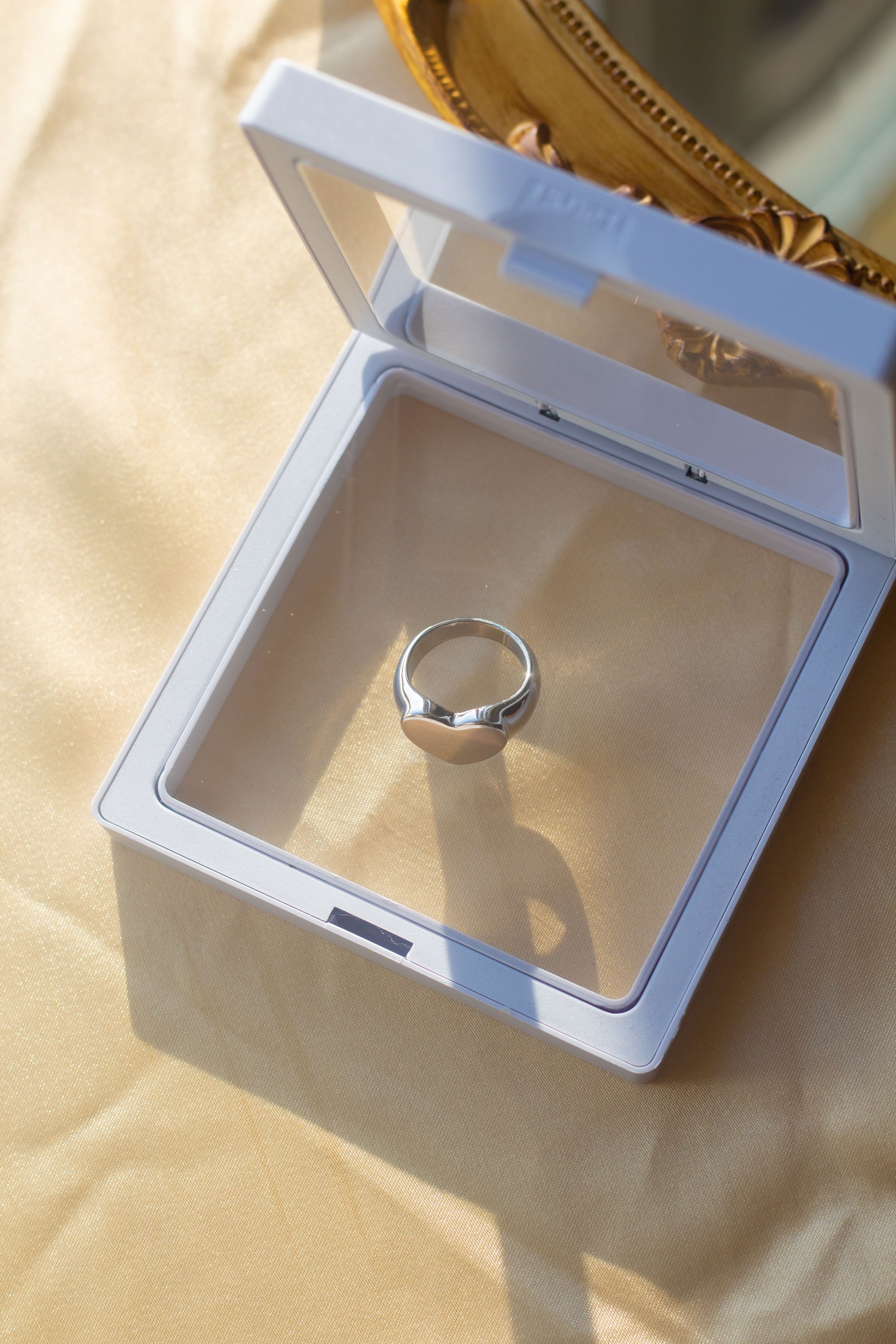 18k silver signet ring resting in a white container on a table with a beige cloth. Ellina Heart Signet Ring by E's Element.