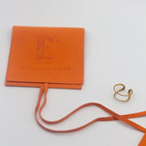 18k gold spiral ear cuff on the right. On the left is an orange leather pouch with the E's Element Logo engraved. Unisex Spiral Ear Cuffs - E's Element.
