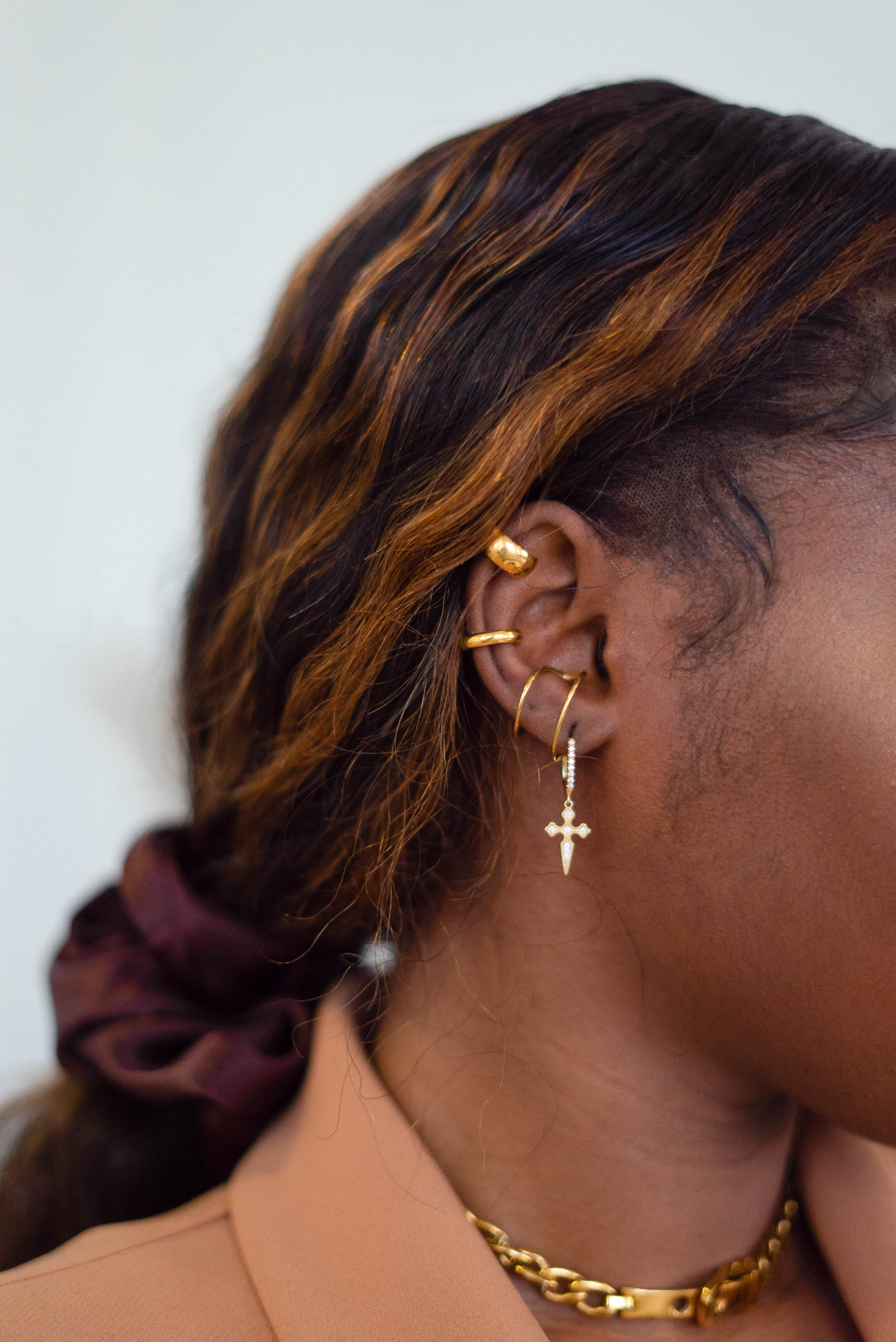 Model wearing 18k gold cuff earrings. The model is also wearing four other earrings and one of them has a cross charm. The model is also wearing an 18k gold chain necklace. Ellina Ear Cuffs by E's Element.