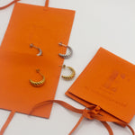 18k gold croissant shaped earrings placed in orange leather pouches. Thick Croissant Stud Earrings - E's Element.