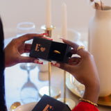 Model in a red jacket holding a black container with the E's Element logo and a heart in gold. Inside the container is an 18k gold ring. Valentine's Day Ring Box (Add-On) - E's Element.