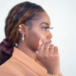 Woman in a light brown suit wearing Criss Cross Cubic Zirconia Ring by E's Element. She is also wearing an 18k gold stainless steel chain bracelet and earrings.
