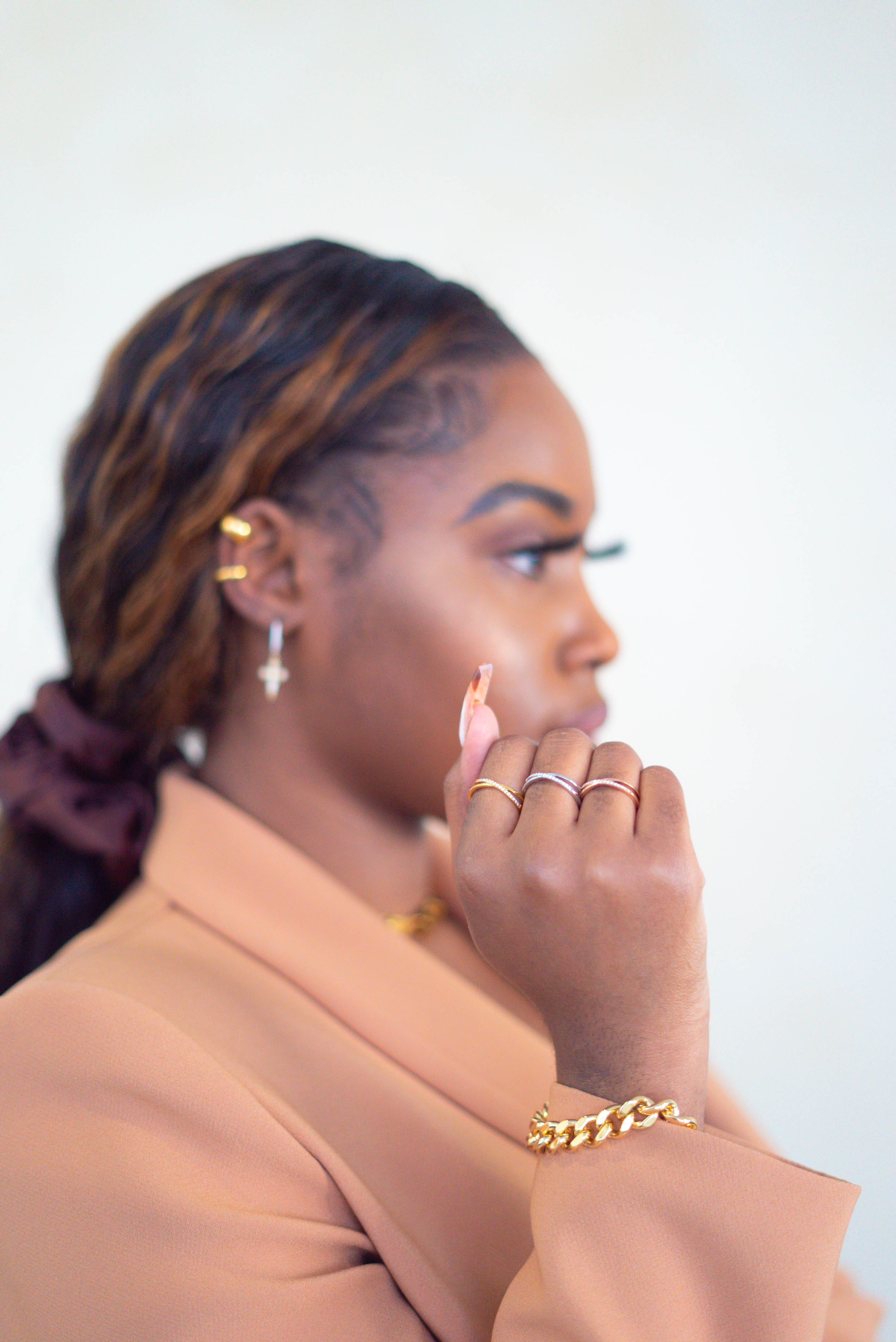 Woman in a light brown suit wearing Criss Cross Cubic Zirconia Ring by E's Element. She is also wearing an 18k gold stainless steel chain bracelet and earrings.